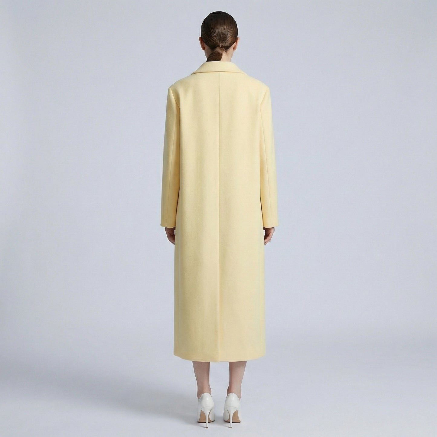 Person wearing a long light yellow coat on a plain background