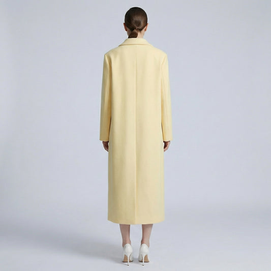 Person wearing a long light yellow coat on a plain background