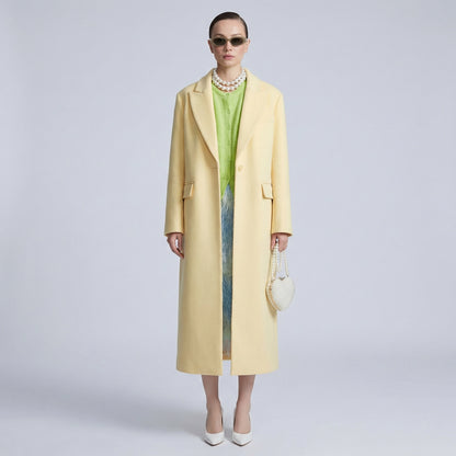 Woman wearing a long yellow coat over a green dress on a light gray background