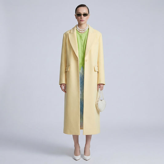 Woman wearing a long yellow coat over a green dress on a light gray background