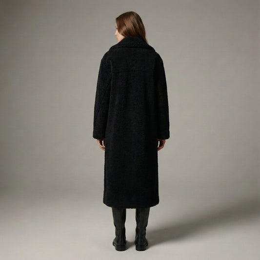 Person wearing a black coat standing against a plain background