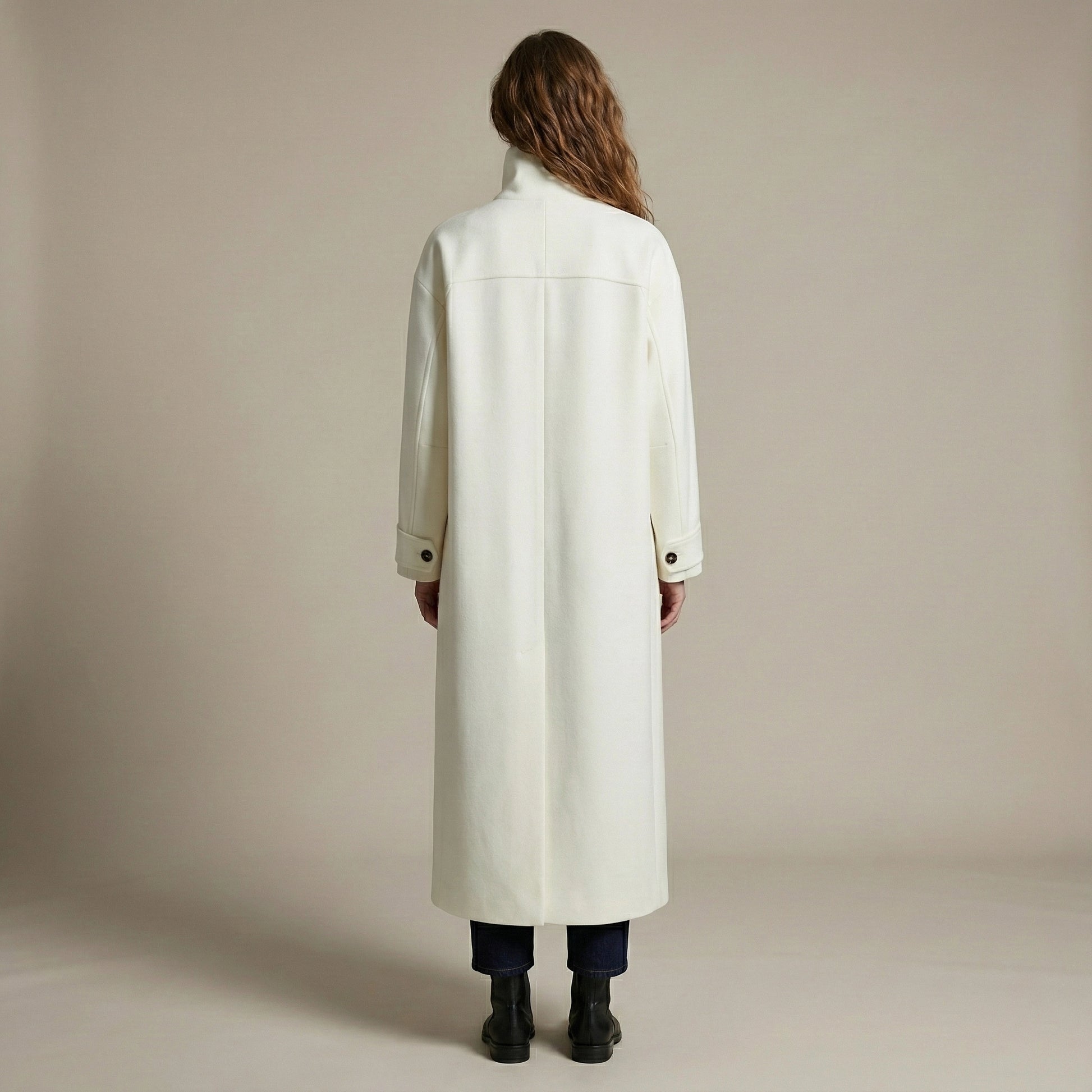 Person wearing a long white coat against a plain background